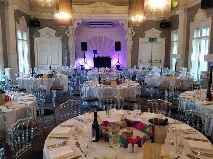 Round dinner tables set under a lit arch with the DJ booth visible in the background at a private event
